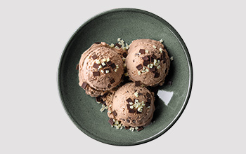 Drei Kugeln Eis in einer Schüssel mit Blättern aus Vollmilchschokolade und Splittern aus weißer Schokolade.